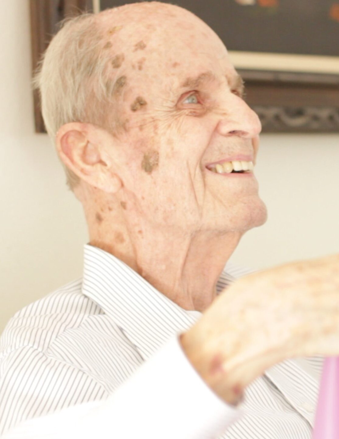 Close-up profile portrait of a smiling elderly man in a striped shirt.