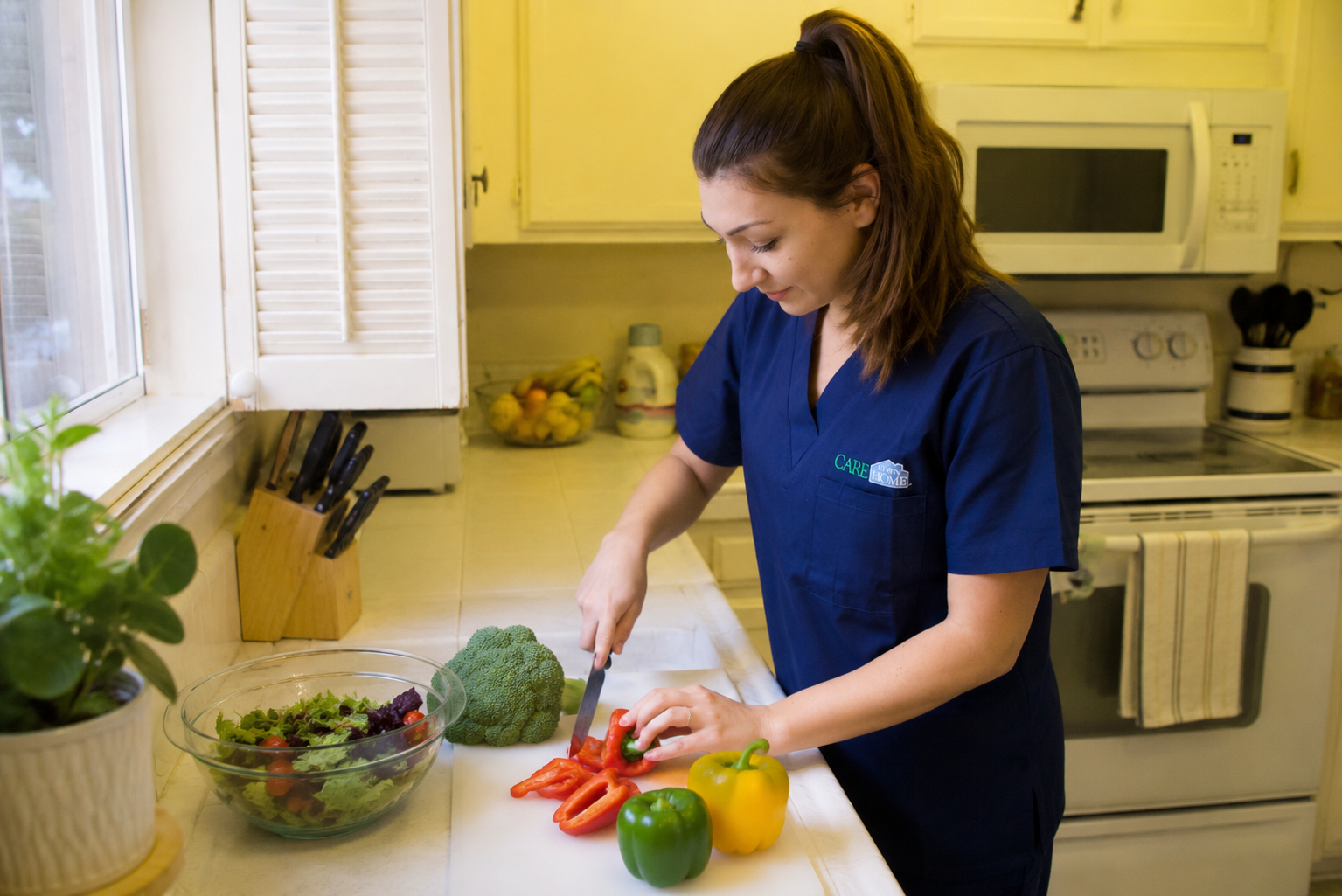 Caregiver in navy scrubs chopping fresh vegetables to prepare a meal in a home kitchen.