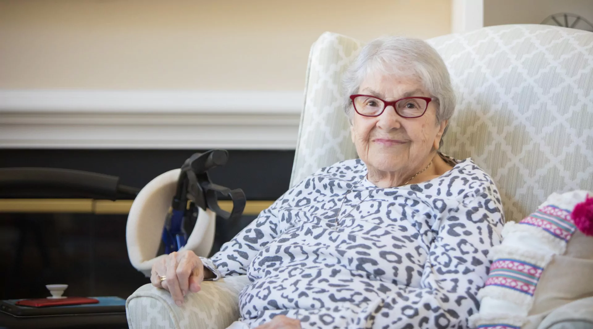 Happy senior woman sitting comfortably in an armchair at home with a walker nearby
