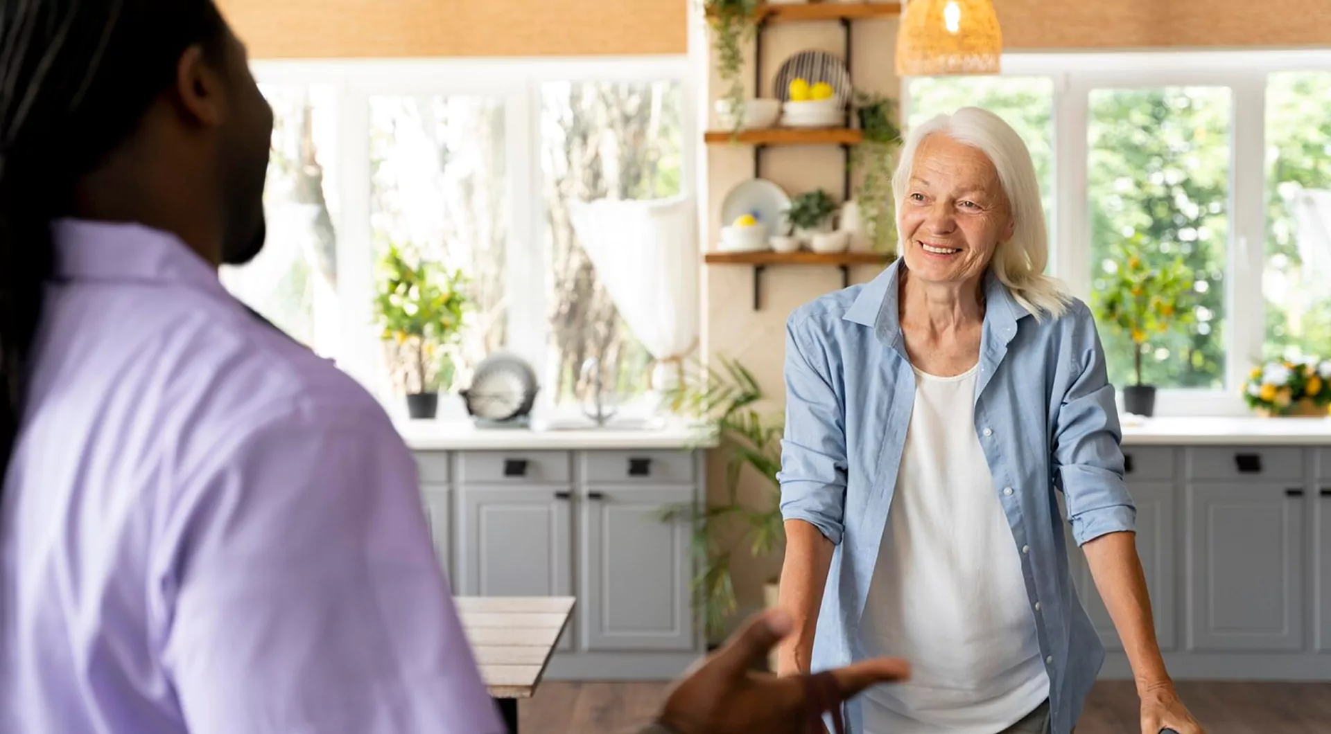 Caregiver talking with a smiling senior woman in her kitchen - Care to Stay Home FAQs