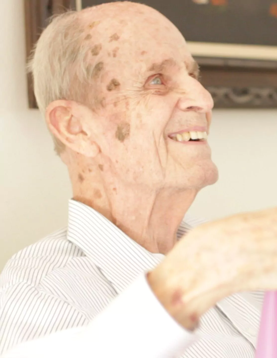 Close-up profile portrait of a smiling elderly man in a striped shirt.